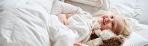 Glad lille pige ligger i sengen med sin bamse og sin Ringsted Dun baby & junior dyne og hovedpude